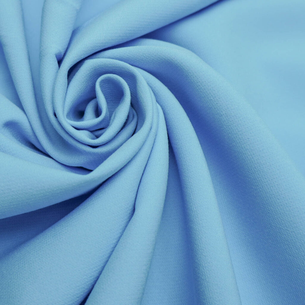 Crepe de alfaiataria azul-claro disposto em dobras em espiral, mostrando a textura do tecido.
